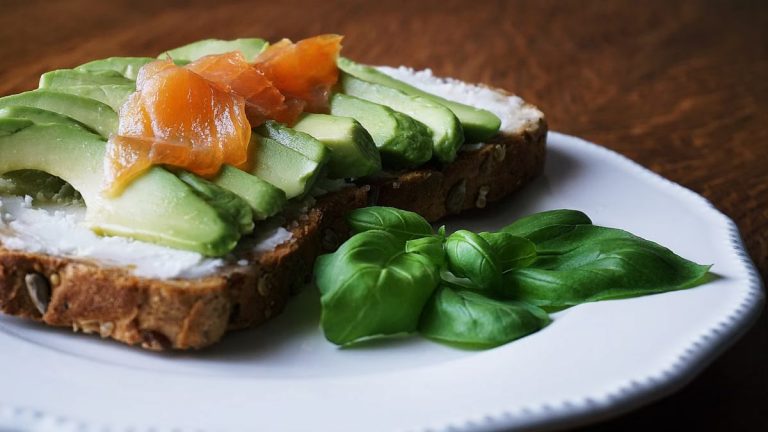 A delicious, healthy meal with avocado and smoked salmon on seeded bread, garnished with basil leaves.